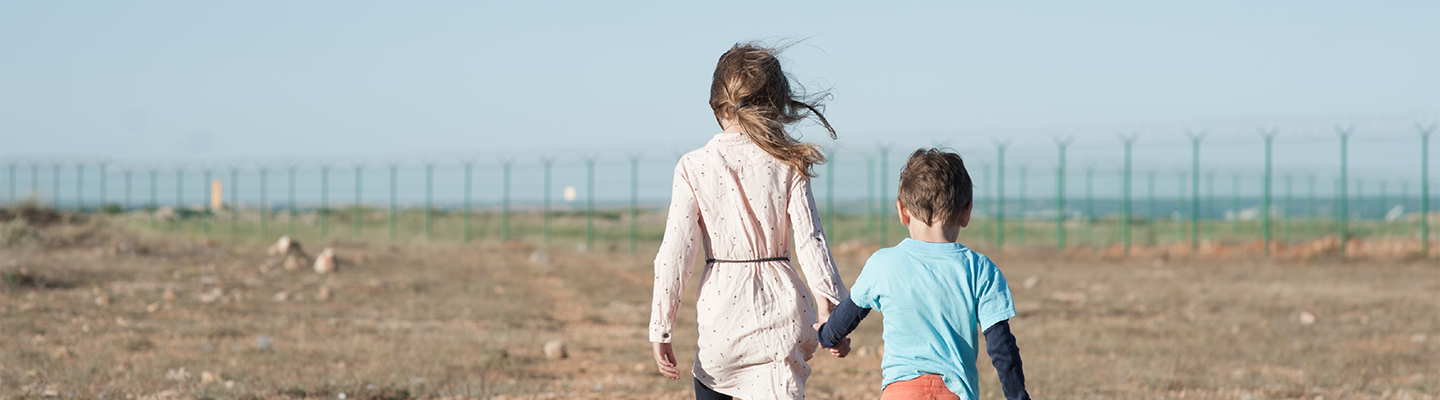 Two children holding hands walking towards fence
